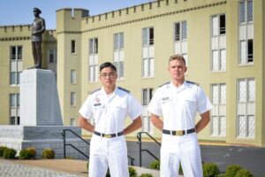 Two male cadets pose in white class uniform in front of the Marshall statue.