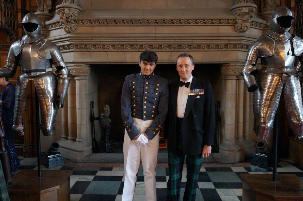 Milenski and Bailey standing in front of fireplace flanked by two suits of armor