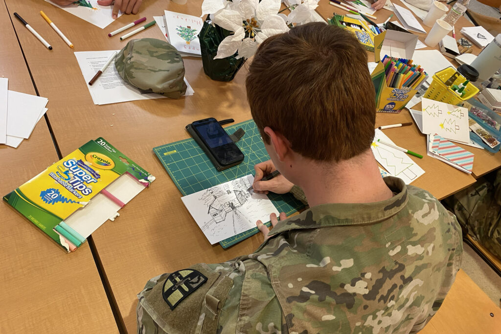 Cadet sits at table with art supplies.