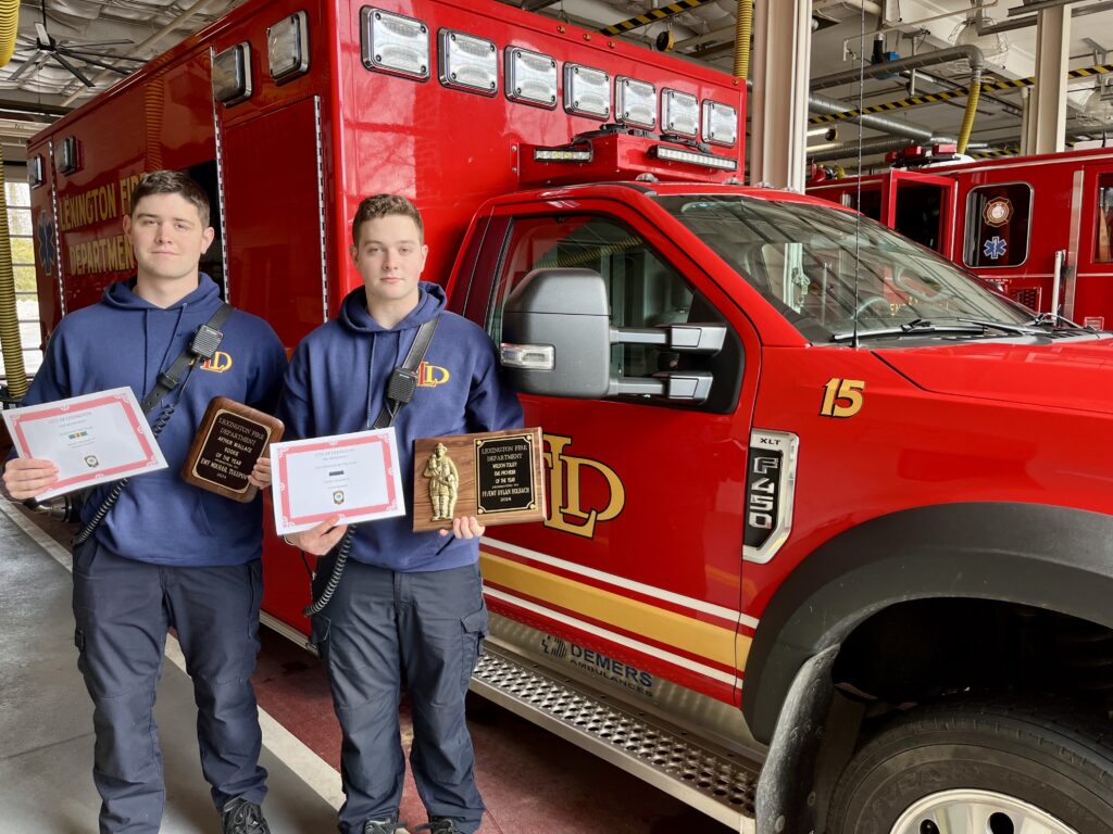 Two cadets stand in front of a fire truck holding certificates.