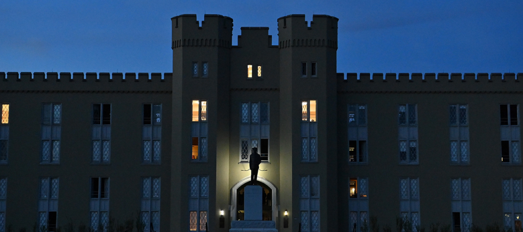 A nighttime view of the VMI Barracks, with lights on in the building.