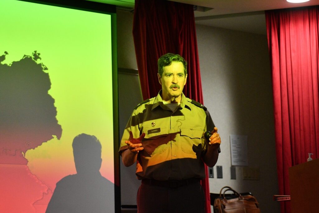 Col. Sunnen stands in front of a screen,