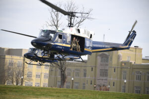 A helicopter flies onto parade ground in front of barracks.