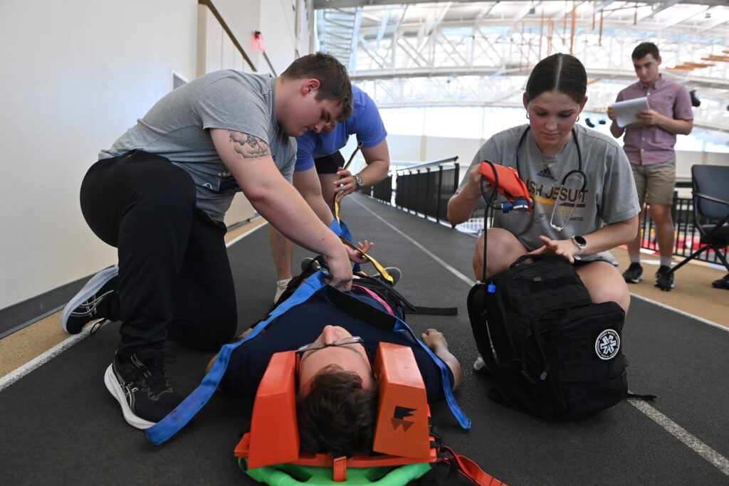 Cadets strap their peer to a spine board to immobilize him before transport during a scenario-based drill in the Corps Physical Training Facility.
