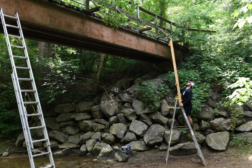 Lawrence Porter '24 sets up equipment to run tests on serviceability of a footbridge on the Cheesie Trail.