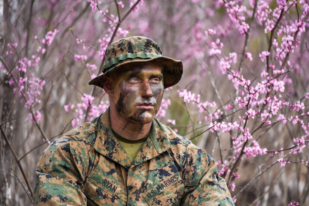 A U.S. Marine Corps recruit in uniform stands centered, surrounded by blooming pink redbud flowers.
