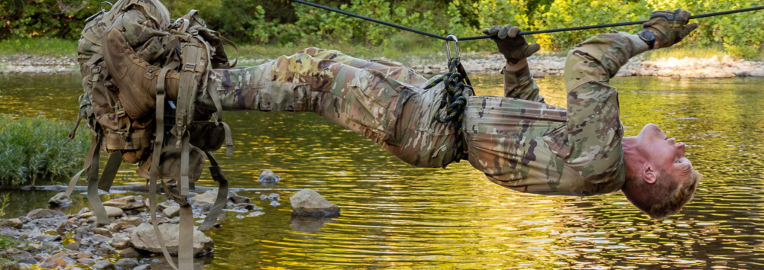 Cadet dangles across a stream hanging onto a rope.